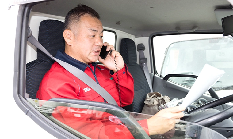 トラックの運転席で書類を見ながら電話をするY.Y.さん