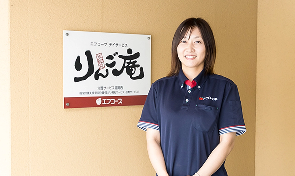 施設入口の壁の前に立つI.J.さん